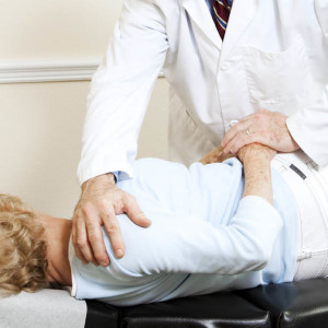 Chiropractor gently adjusting a senior woman's spine.